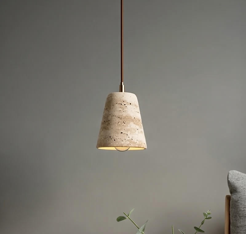 Concrete pendant light hanging against a gray wall with a plant and cushion in the foreground.